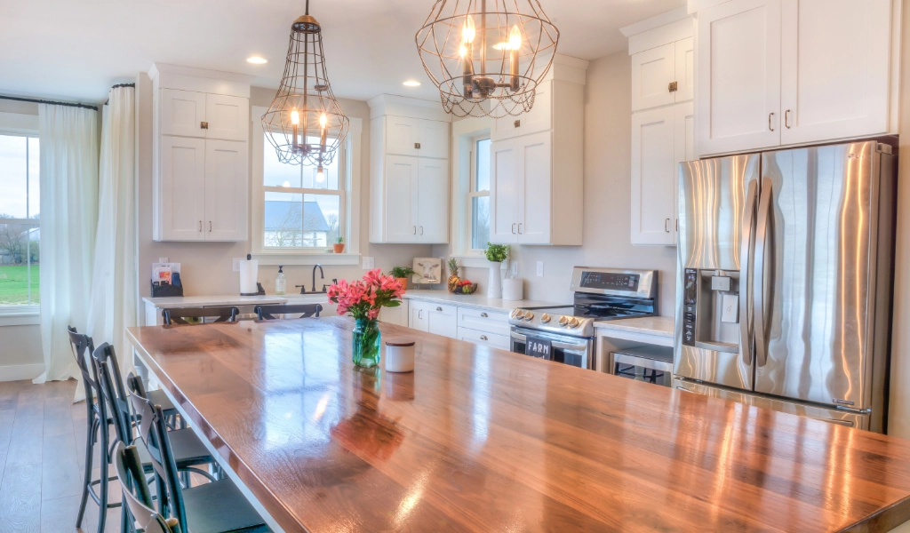 A modern kitchen with white cabinets, stainless steel appliances, a large wooden island with chairs, and hanging light fixtures.