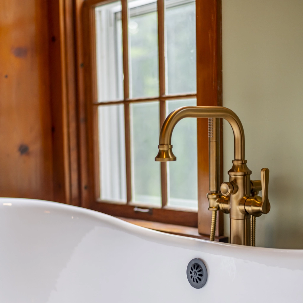 Brass faucet on a brand new tub, sitting in front of a window.