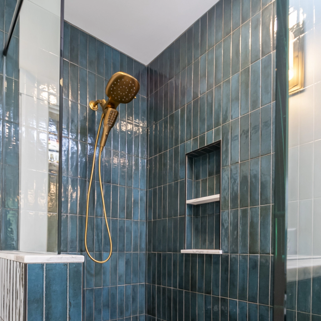A blue tiled shower with brass fixtures, newly renovated by a home remodeling company.