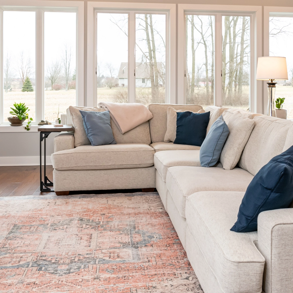 Newly renovated living room with large windows, comfortable couch, and colorful rug.