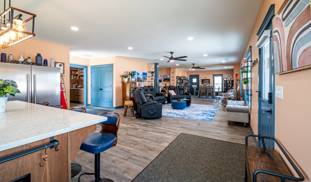 Open-concept living space with a kitchen island, lounge area, blue accents, modern furnishings, wood flooring, and decorative wall art—an award-winning home addition designed for style and comfort.