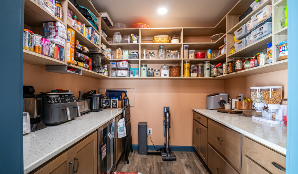 A well-organized pantry with shelves holding food items, appliances on countertops, and storage containers neatly arranged along the walls—an award-winning home addition designed for both style and efficiency.