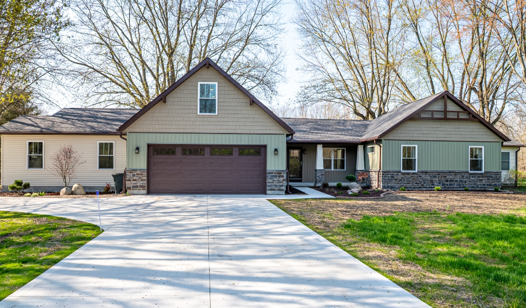 Single-story suburban house with a gabled roof, attached garage, wide driveway, and a lawn with some trees in the background—an award-winning home remodel & additions enhance its comfort and curb appeal.