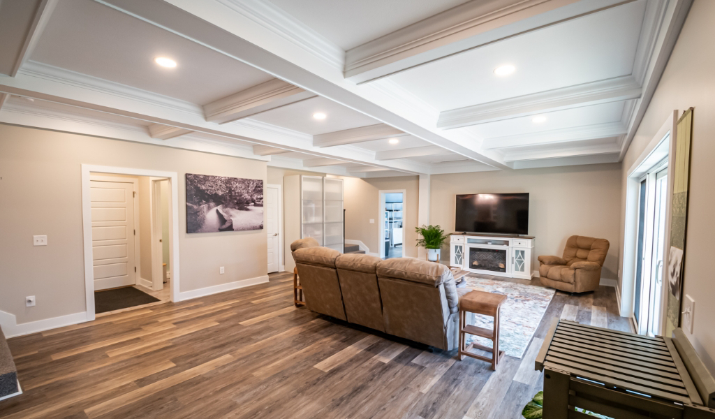 Modern living room from an award-winning home remodel & additions, featuring wood flooring, beige walls, recessed lighting, a large TV, brown couches, a recliner, and glass doors leading outside.