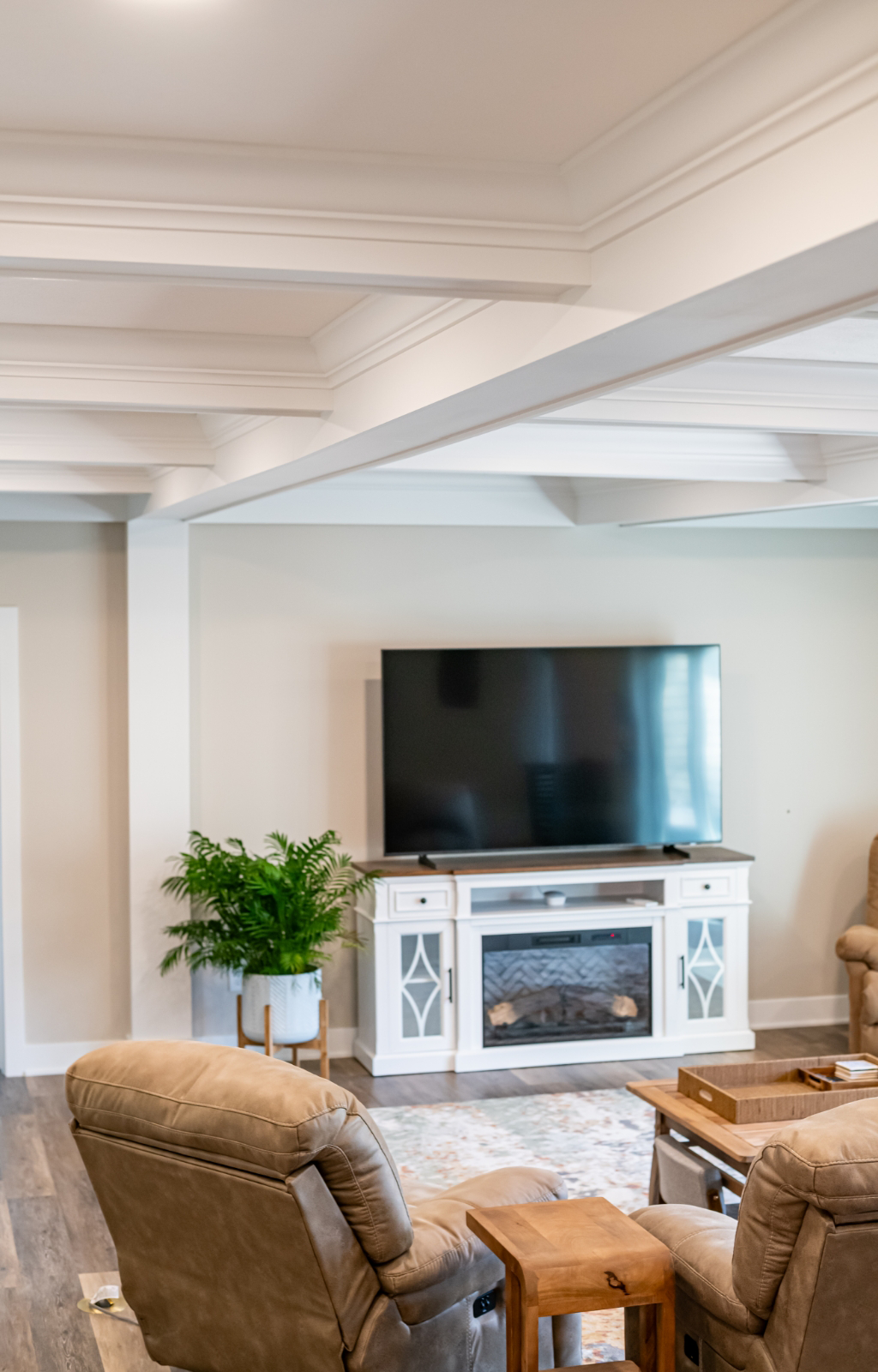 A living room with beige recliners, a wooden coffee table, a TV on a white stand, a potted plant, and hardwood floors showcases an award-winning home remodel & additions.