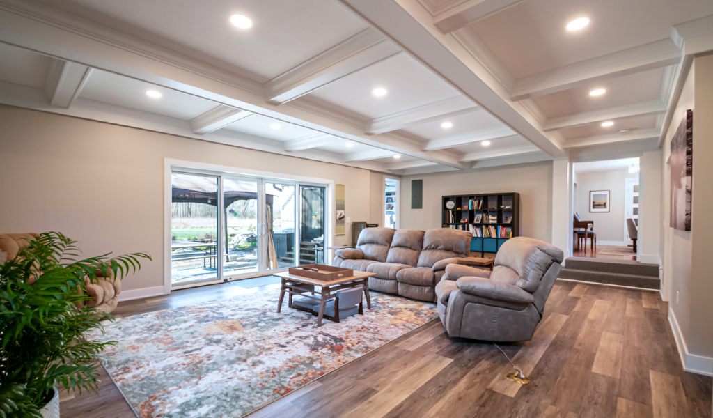A spacious living room with a large rug, reclining sofas, a coffee table, bookshelves, wood flooring, and sliding glass doors leading to an outdoor patio—part of an award-winning home remodel & additions.