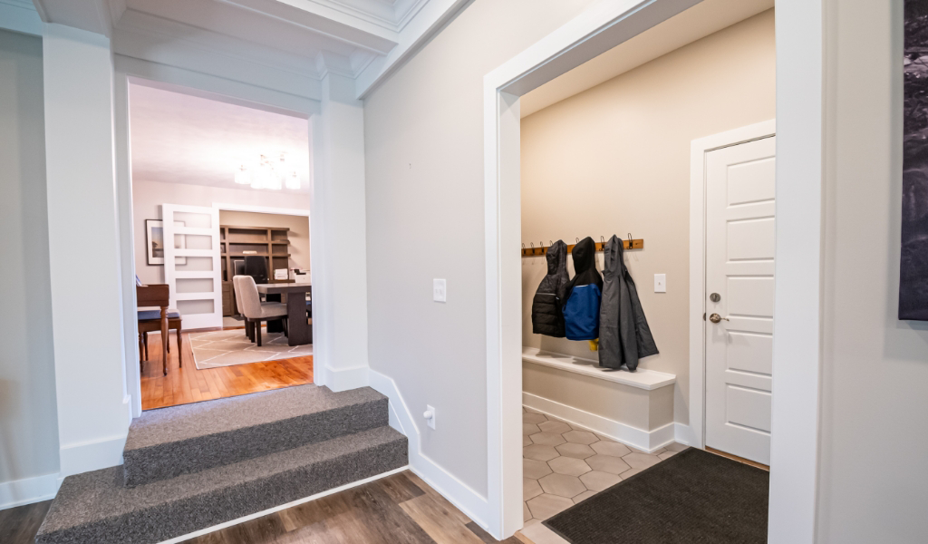 Entryway with a small mudroom area featuring a bench, coat hooks with jackets, and a white door—part of an award-winning home remodel & additions—plus an adjacent hallway leading to the dining room and office.